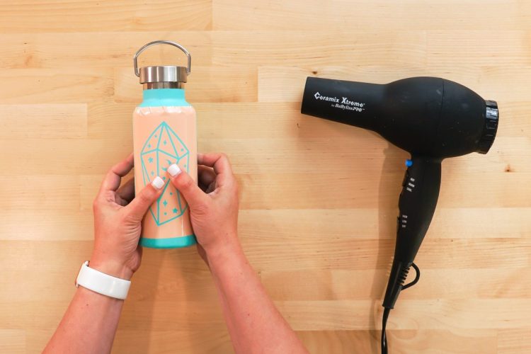 Hands using a blow dryer to heat up the stencil