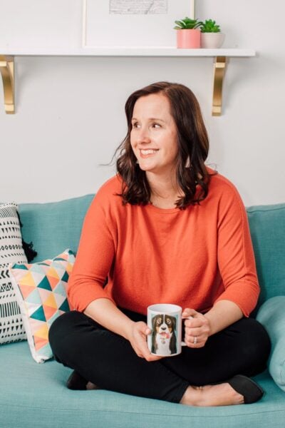 Cori sitting crossed legged on a couch and holding a coffee mug