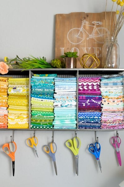 A shelf filled with fabric and scissors hanging on hooks below the shelf