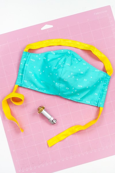 Picture of a completed face mask lying on a pink FabricGrip Cricut mat along with the Cricut rotary blade tool.