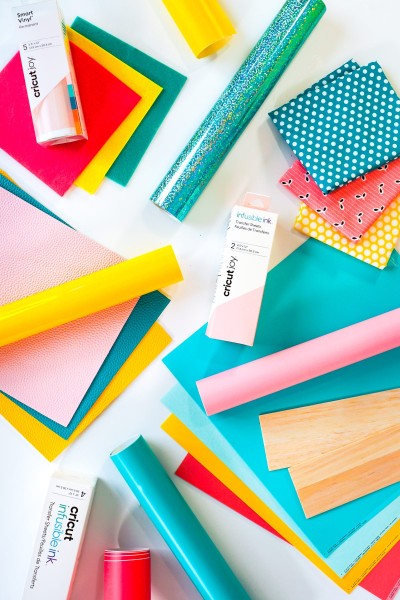 Flat lay of dozens of Cricut materials in pink, teal, and yellow