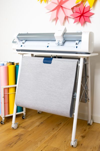 Cricut Venture on Cricut Venture Docking Stand with colorful paper stars and rolls of material in a cart next to it.