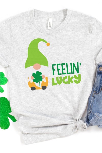 Blue jean shorts and shamrock shapes along with a gray t-shirt that has a gnome holding a four leaf clover and the words Feelin' Lucky