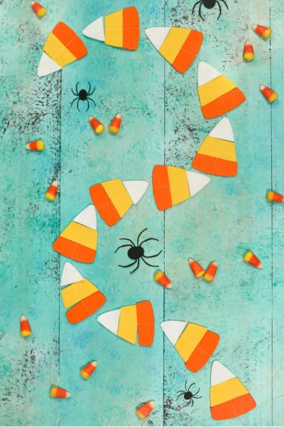 Real candy corn candy, paper cut black spiders and a candy corn garland lying on an aqua blue table