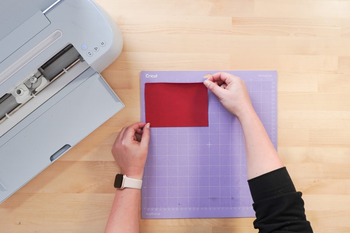 Hands putting leather on the Cricut mat.