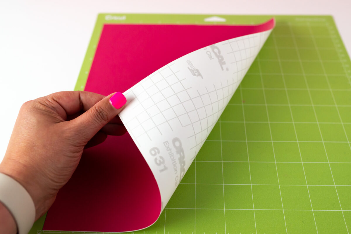Hand showing adhesive vinyl paper carrier sheet down on mat