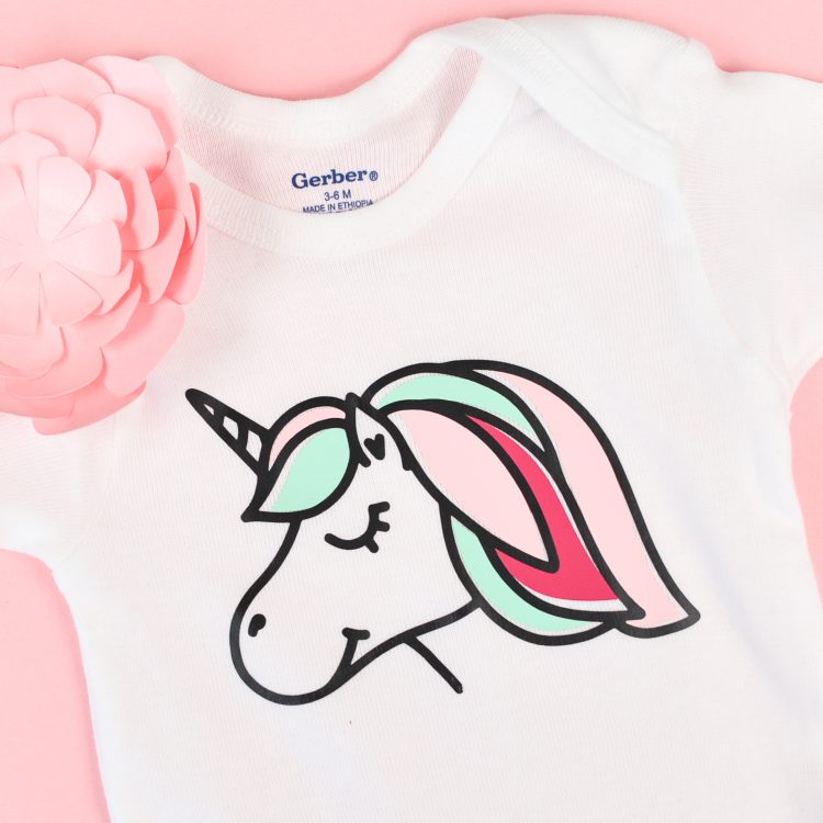 A close up of a pink paper cut flower and a white onesie with an image of a unicorn on it