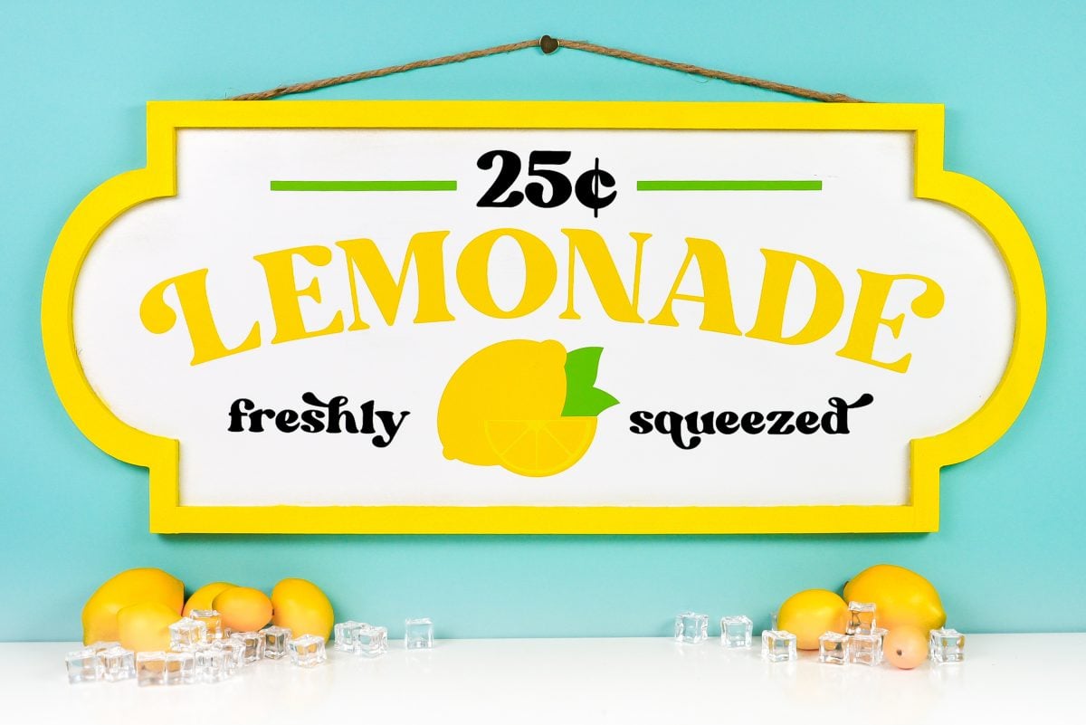 Finished lemonade stand sign on teal background styled with faux lemons and ice