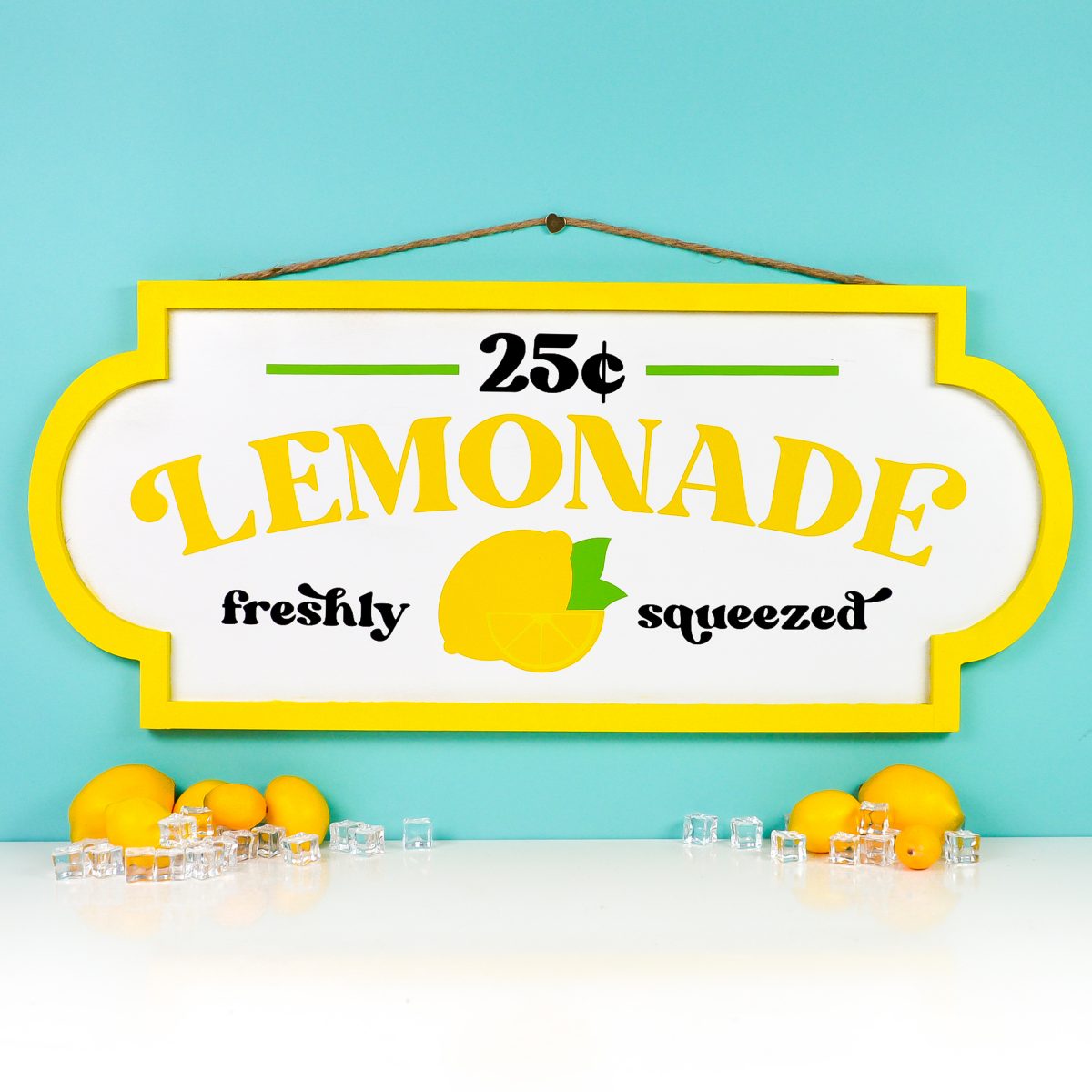 Finished lemonade stand sign on teal background styled with faux lemons and ice