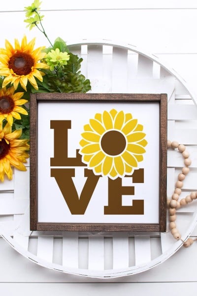 Wooden beads, a bunch of sunflowers and a wooden framed picture of the word love with the letter 'O' as a sunflower, all attached to a white basket hanging on wall