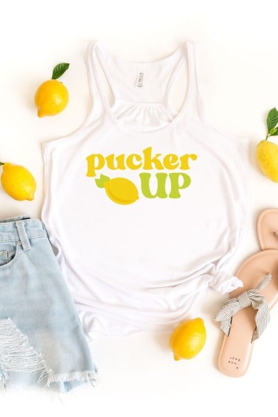 Blue jean shorts, a pair of sandals and four lemons arounds a white tank top that has an image of a lemon on it and the saying Pucker Up