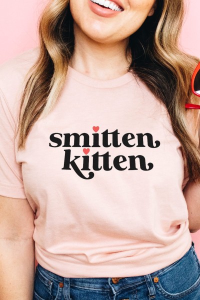 Girl holding a pair of heart-shaped red sunglasses and wearing a pink t-shirt that says, smitten kitten