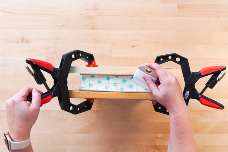 Hands scraping the transfer tape onto a stenciled design
