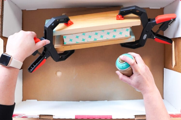 Hands holding a book with a star stencil on it and clamps in a box getting ready to spray paint the edges