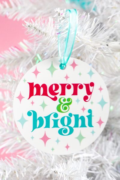 Colorful "merry & bright" ornament on a white Christmas tree with a pink background
