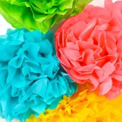 A close up of four paper cut flowers, in blue, green, yellow and pink