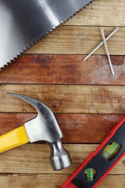 A saw, hammer, nails and level sitting on top of a wooden table