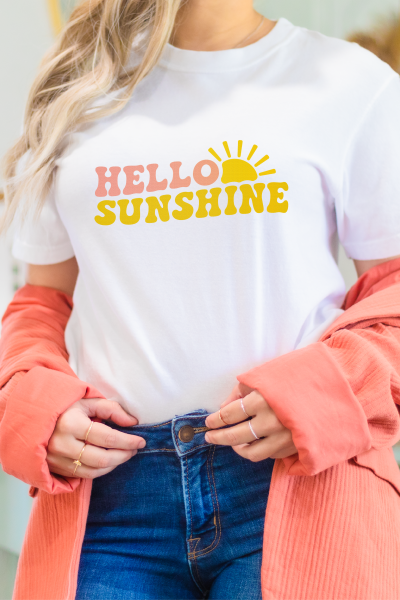 Woman wearing blue jeans, a coral colored sweater and a white t-shirt that says Hello Sunshine