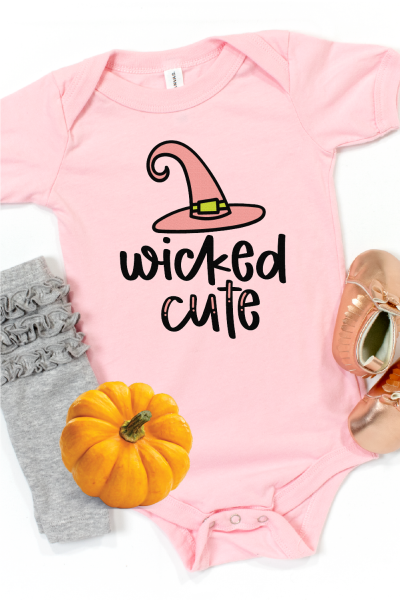 A pair of tiny ruffled gray baby leggings. a pair of baby moccasins, a small orange pumpkin and a pink baby onesie that has a witch's hat on it and the saying, Wicked Cute